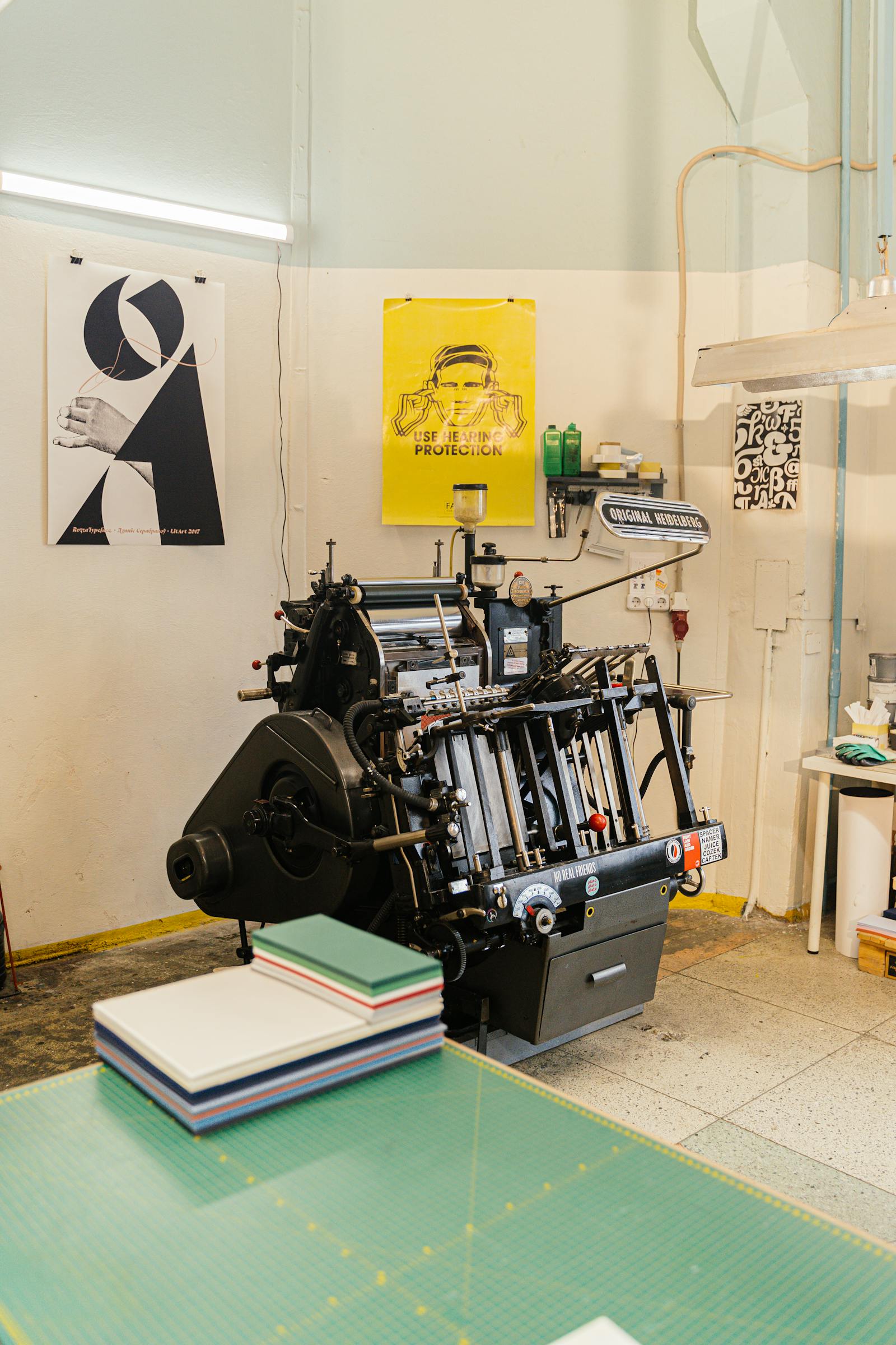 A designer working in a studio with a vintage printing press surrounded by printed posters and design materials.